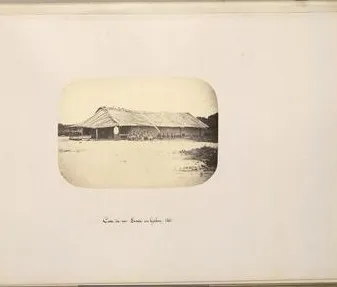 Planche d’album : la case du roi Denis, long bâtiment à toit de feuilles, silhouettes devant l’entrée