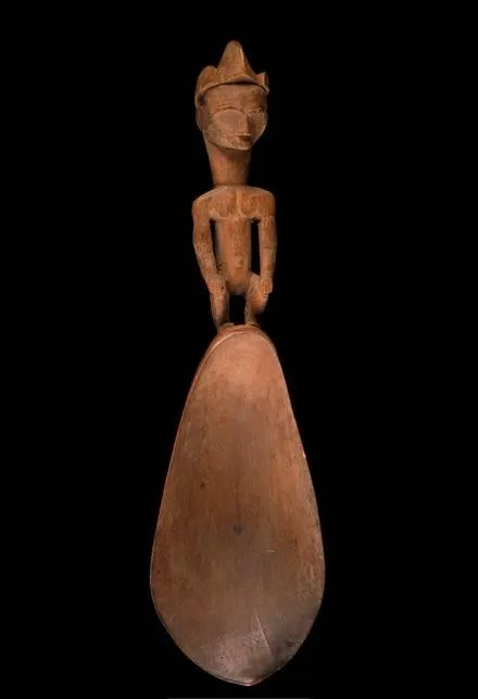 Cuiller de bois brun-rouge dont le manche est un personnage debout sculpté